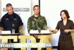 Två manliga soldater och en civilklädd kvinna står på en scen