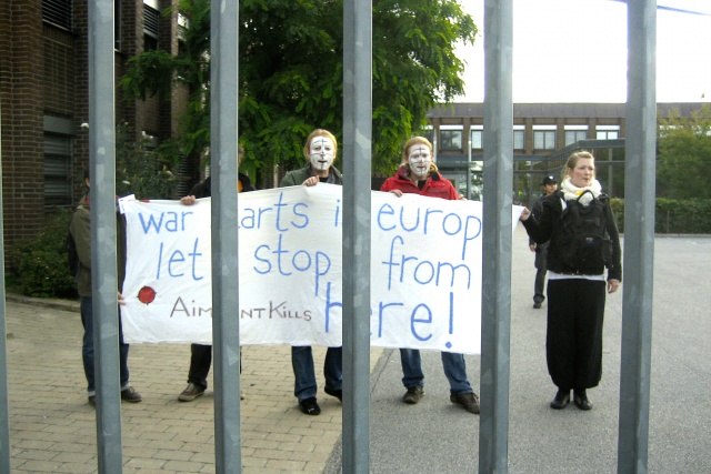4 personer står innanför Aimpints grindar och håller upp en banderoll med texten: War Starts in Europe - Lets stop it from here!