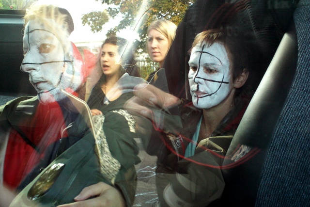 Clownsminkade aktivister reflekteras i en bilruta