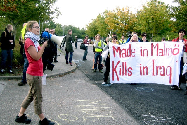 En person pratar i en megafon framför demonstration. Banderoll med texten "Made in Malmö, kills in Iraq"